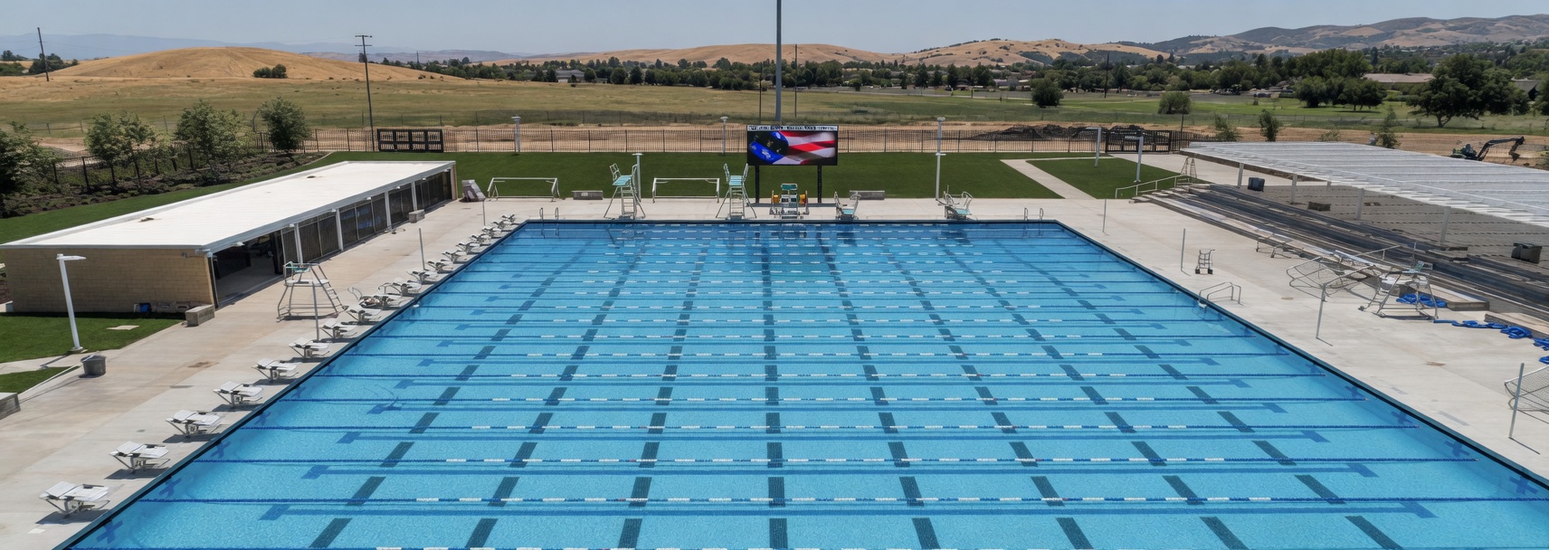 Elk Grove–style 50-meter competition pool with lane lines, starting blocks, bleachers, and shade canopy